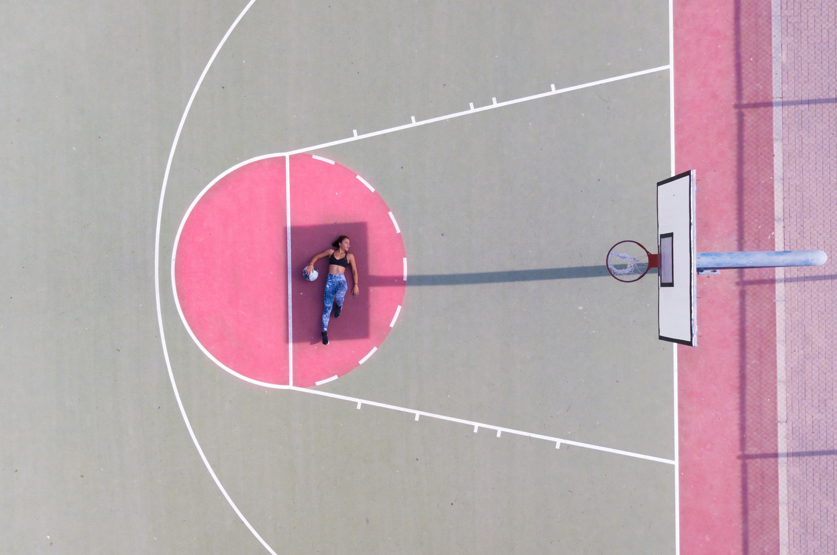Drone shot captures an athlete posing with a basketball on an outdoor court in daylight.