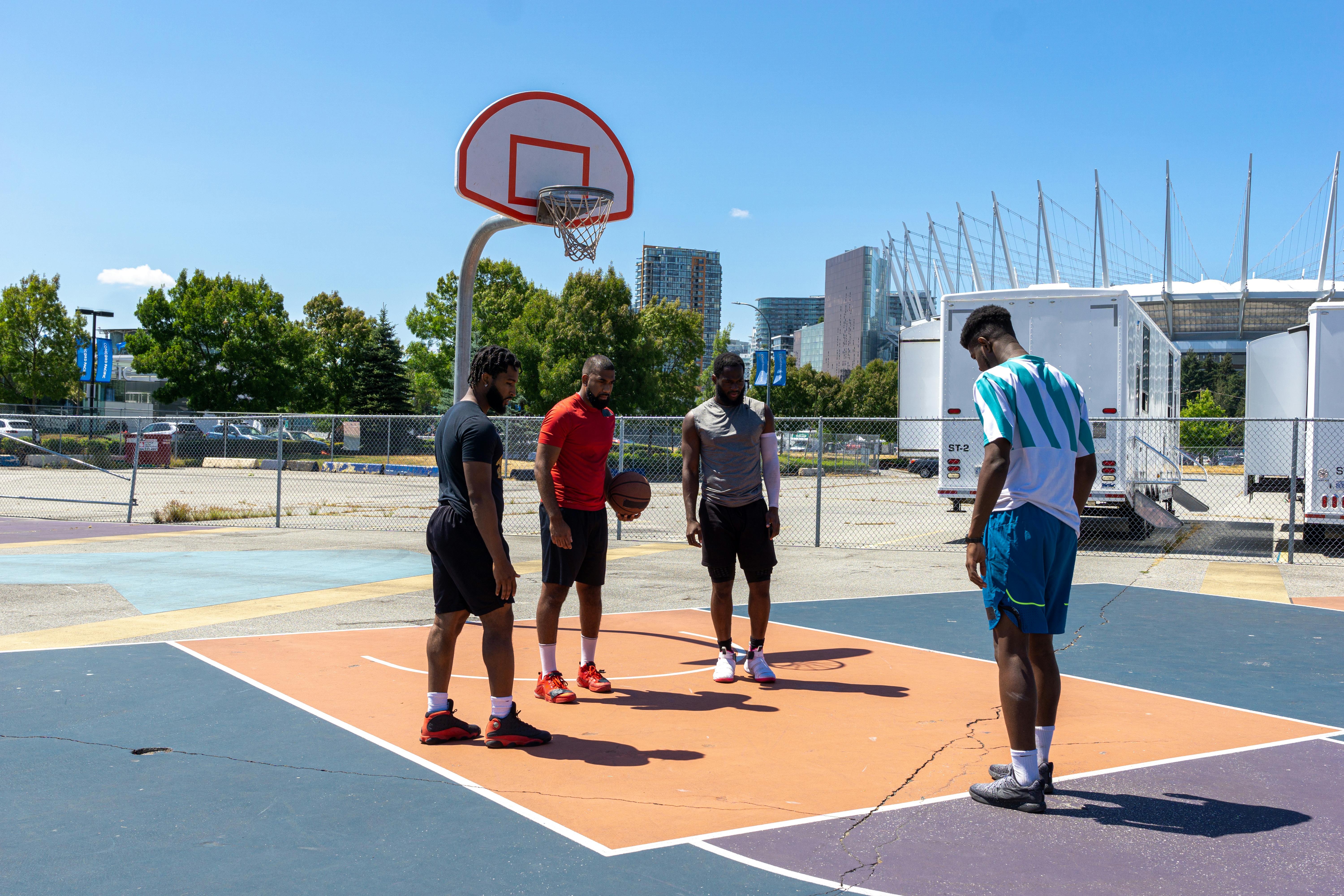 Diverse group of men practicing basketball outdoors in an urban setting.